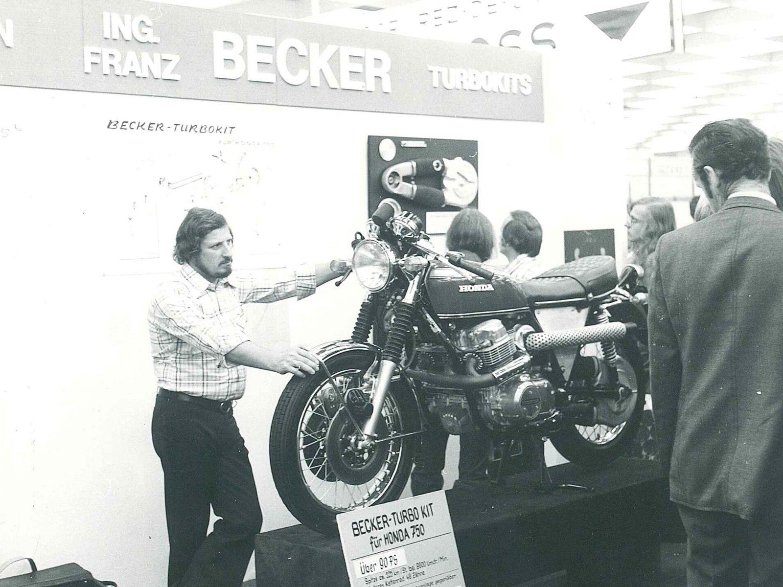 Franz Becker na stoisku targowym Ing. Franz Becker Turbokits w latach siedemdziesiątych, obok Honda CB 750 z zestawem turbo i zwiedzający, zdjęcie czarno-białe