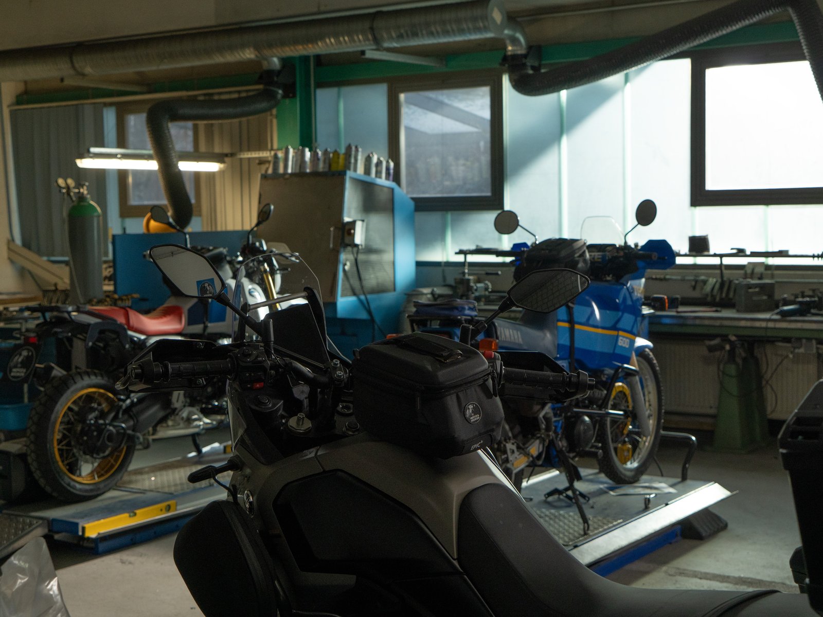 Dział rozwoju Hepco & Becker w Pirmasens, kilka motocykli na podnośnikach warsztatowych, w tym Yamaha Ténéré 700 i skuter z torbą na baku